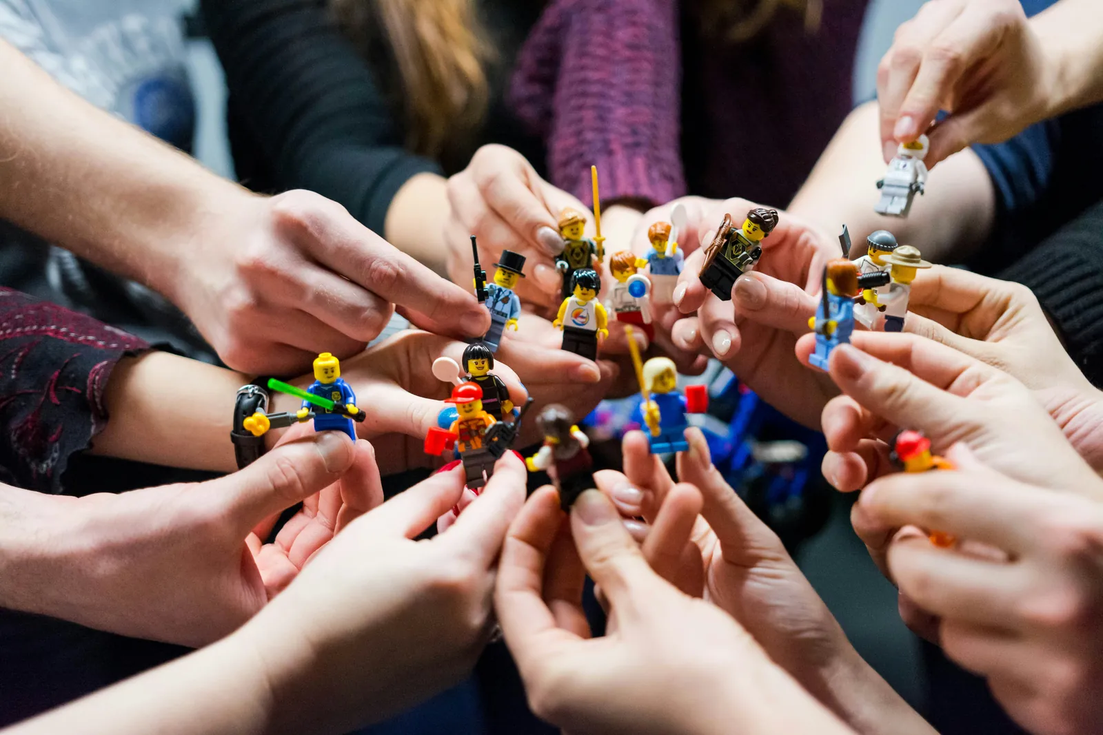Hände halten LEGO-Minifiguren im Kreis – Teamtag-Idee mit spielerischem Einstieg.